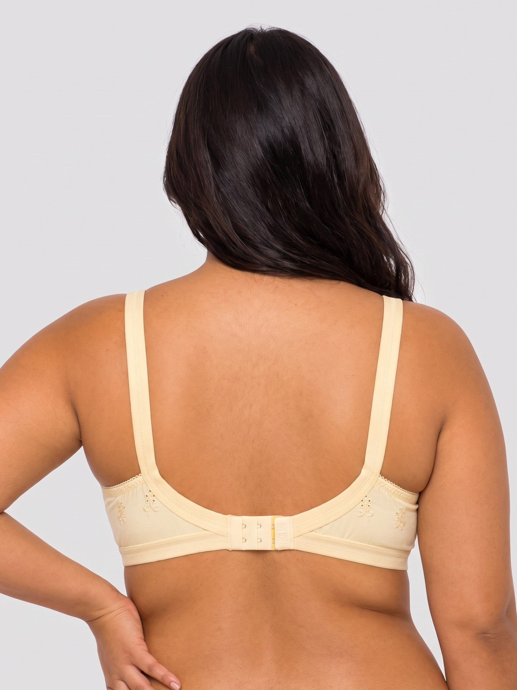 A woman shown from the back wearing a light beige bra with wide straps and a center hook-and-eye closure, against a plain light gray studio background. #color_cream