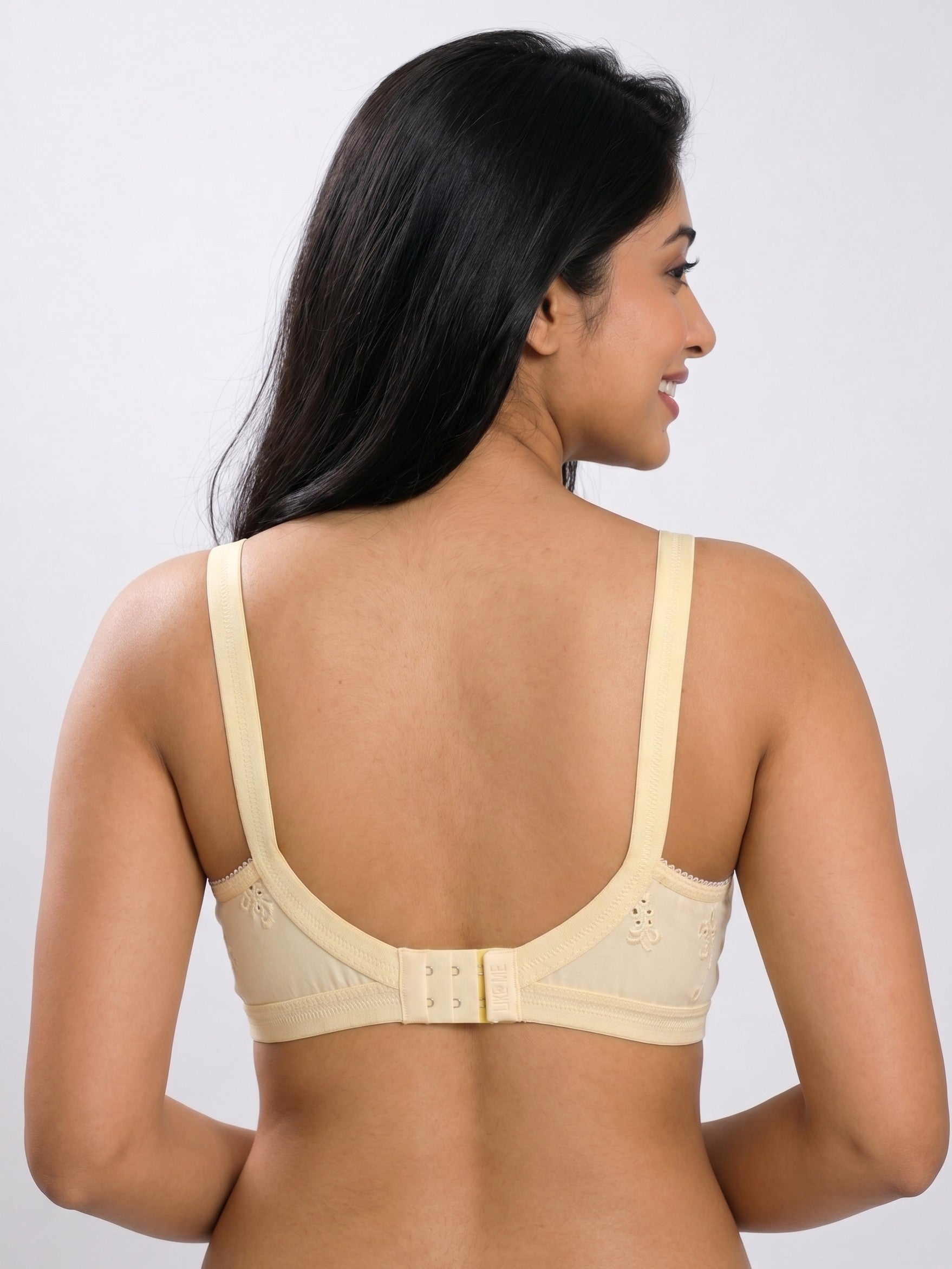 A woman shown from the back wearing a light beige bra with wide shoulder straps and a double-strap back closure, against a plain light gray studio background. #color_cream