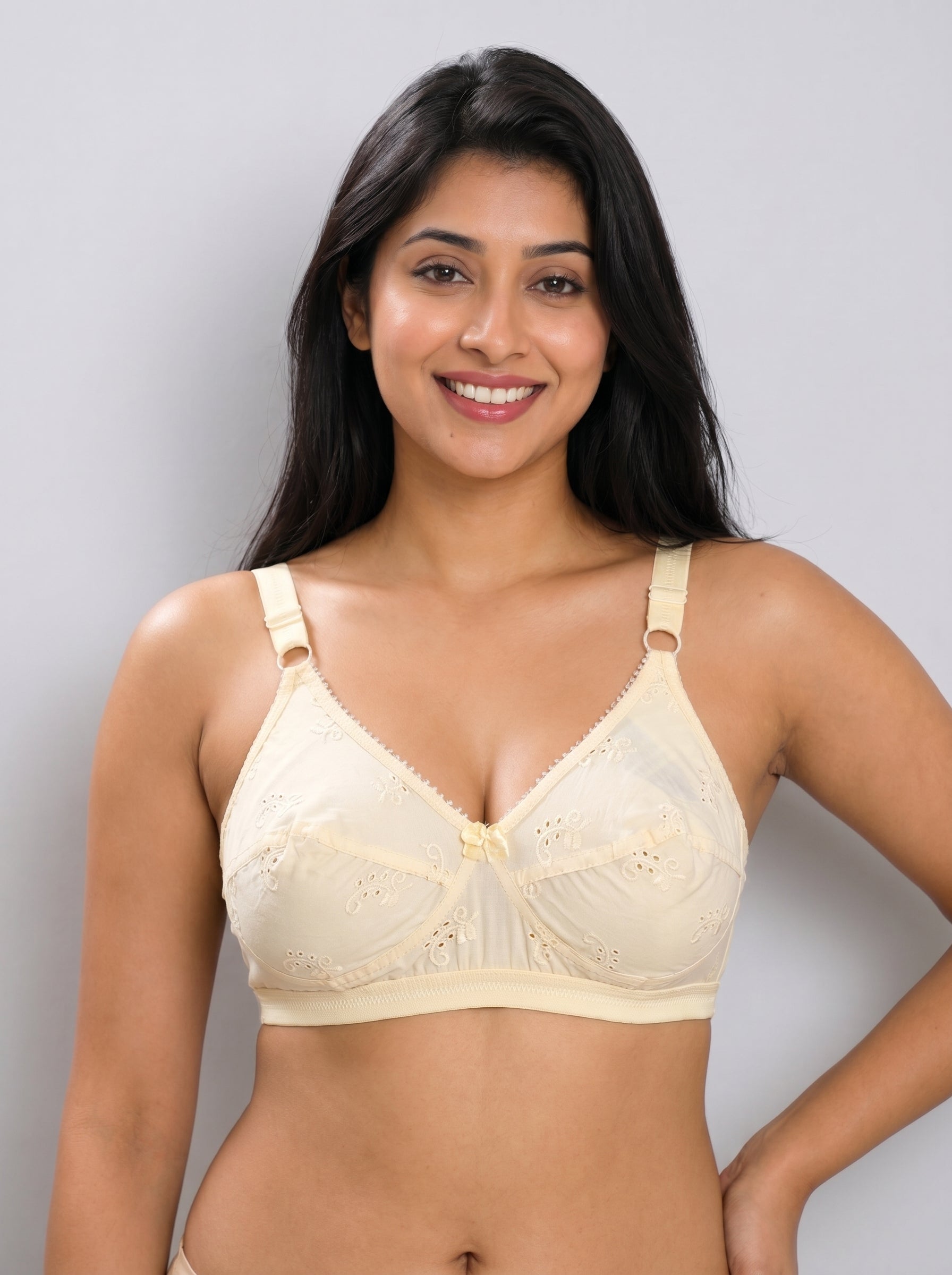 A woman modeling a light beige underwire bra with scalloped edges and lace detailing, set against a plain light gray studio background. #color_cream