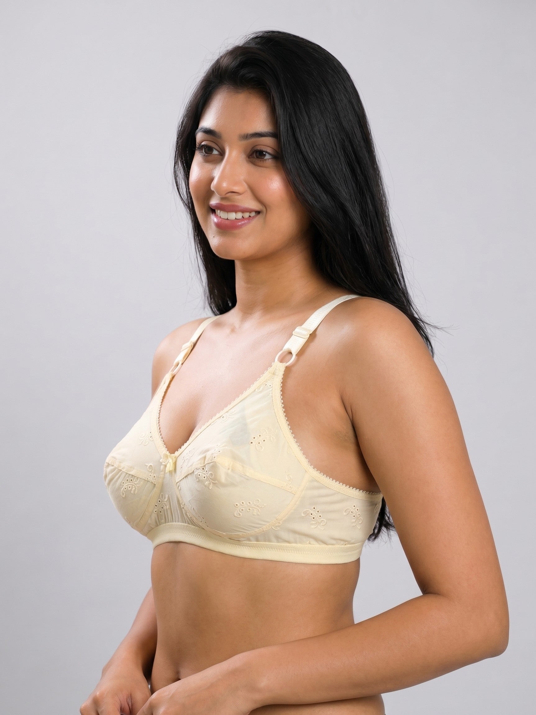 A woman modeling a light beige underwire bra with lace detailing and adjustable straps, set against a plain light gray studio background. #color_cream