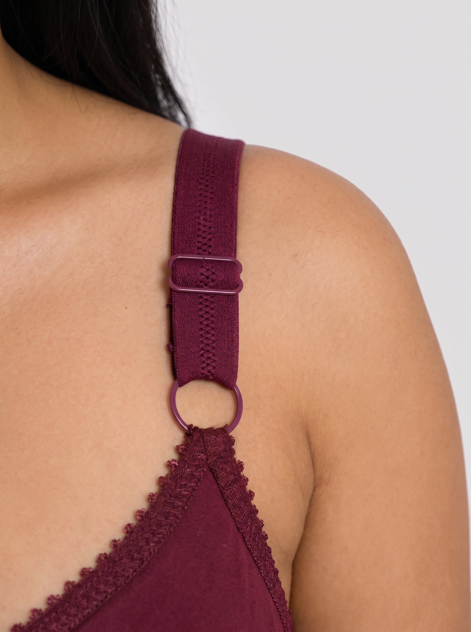 Close-up of a model's shoulder and upper back wearing a burgundy knit bralette with an adjustable strap and metal ring detail. #color_maroon