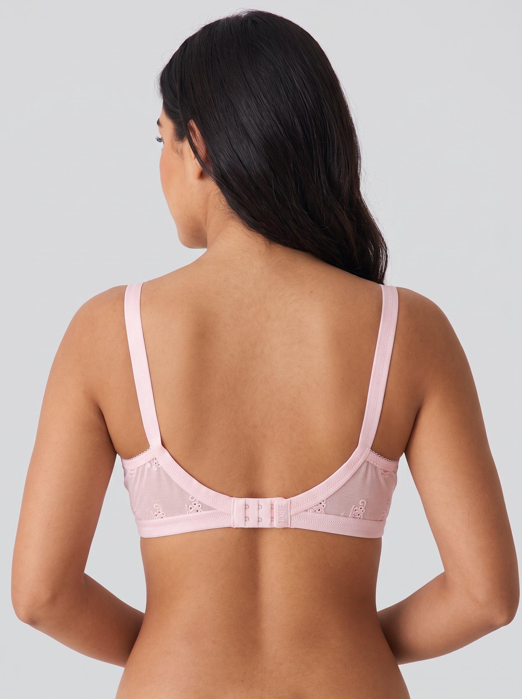 A woman shown from the back wearing a light pink underwire bra with thin straps and a lace-trimmed back panel, photographed against a plain light gray studio background. #color_pink
