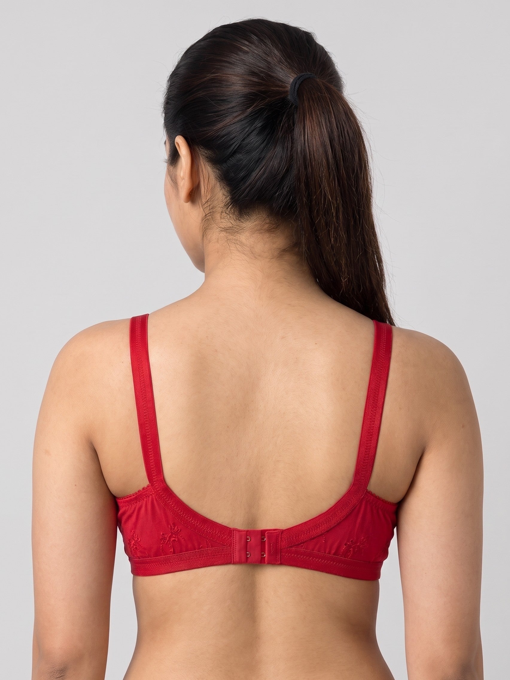 A woman viewed from the back wearing a red bra with wide shoulder straps and a center back strap closure, against a plain light gray studio background. #color_red