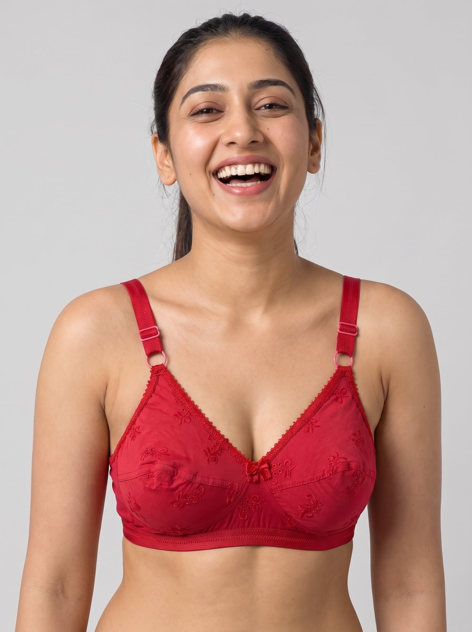A woman smiling and wearing a red lace underwire bra with adjustable shoulder straps against a solid gray background. #color_red