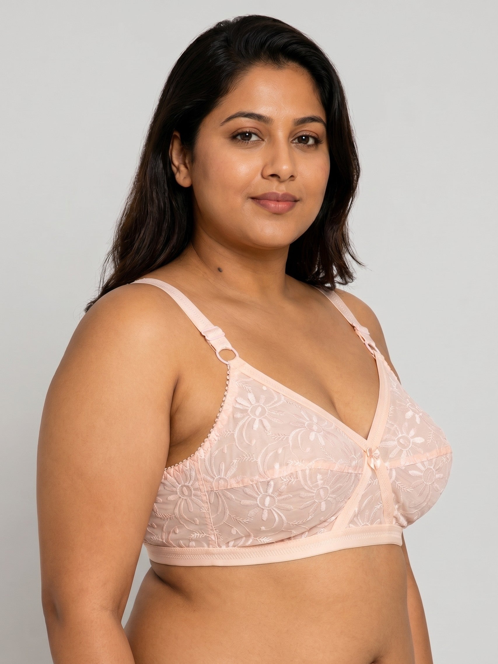Woman wearing a light pink lace bra against a plain background #color_peach