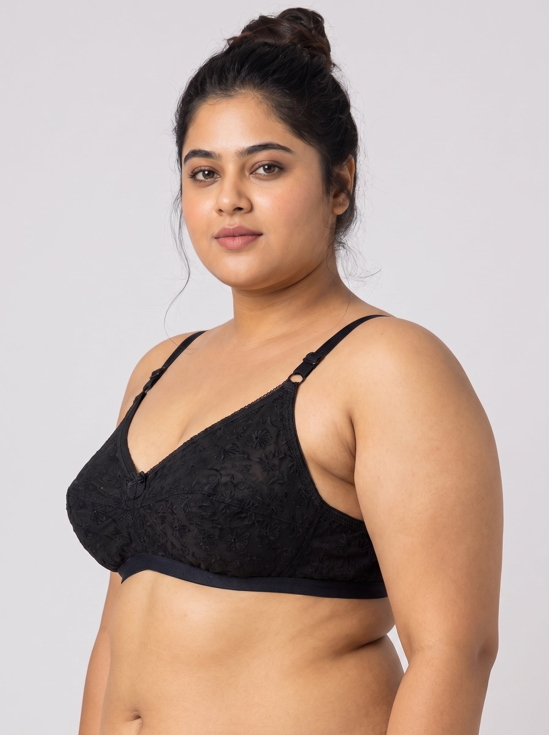 A plus-size woman wearing a black lace underwire bra, photographed against a solid light gray studio background. #color_black