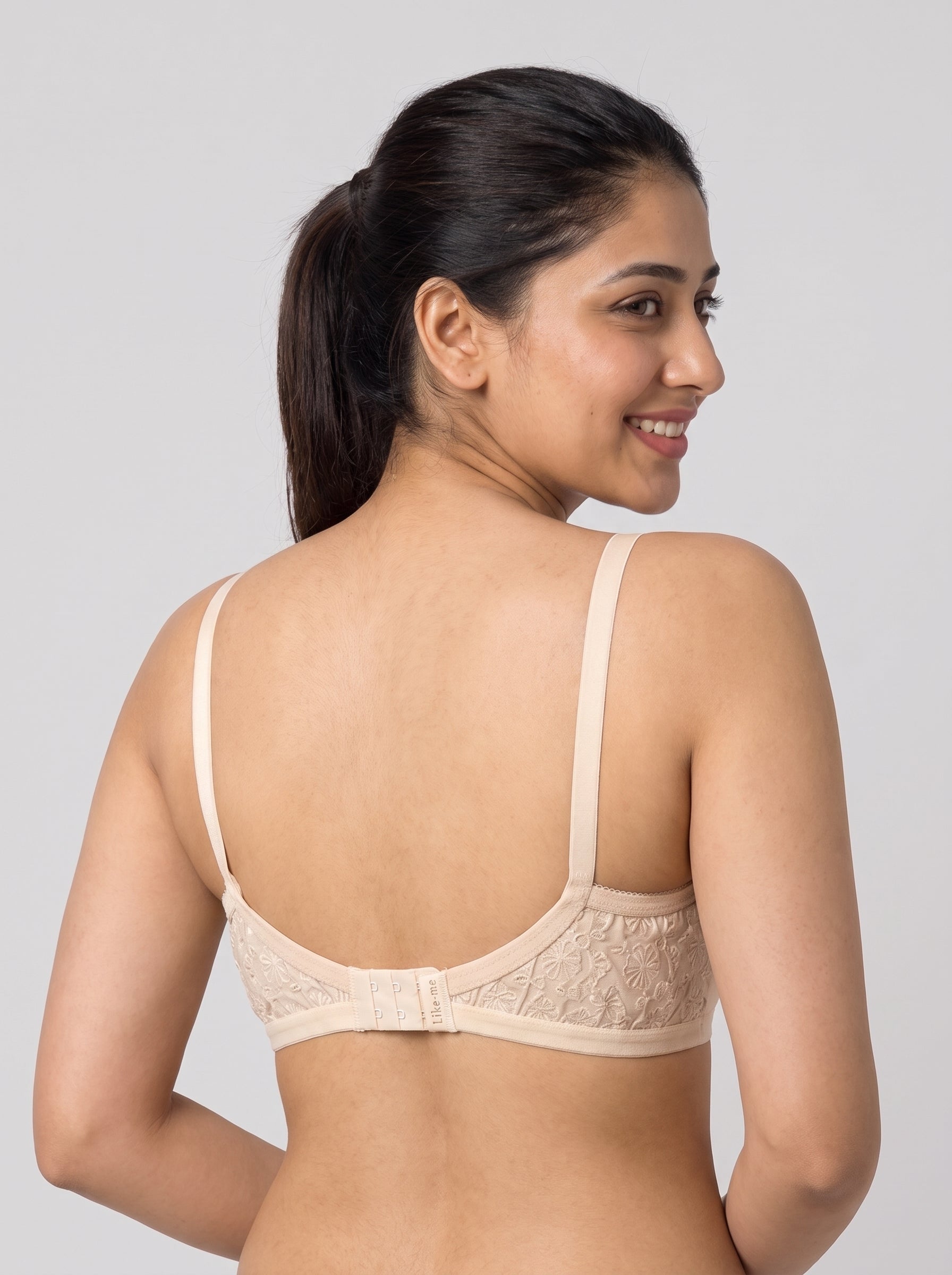 A woman shown from the back wearing a light beige lace underwire bra against a solid gray studio background. #color_cream