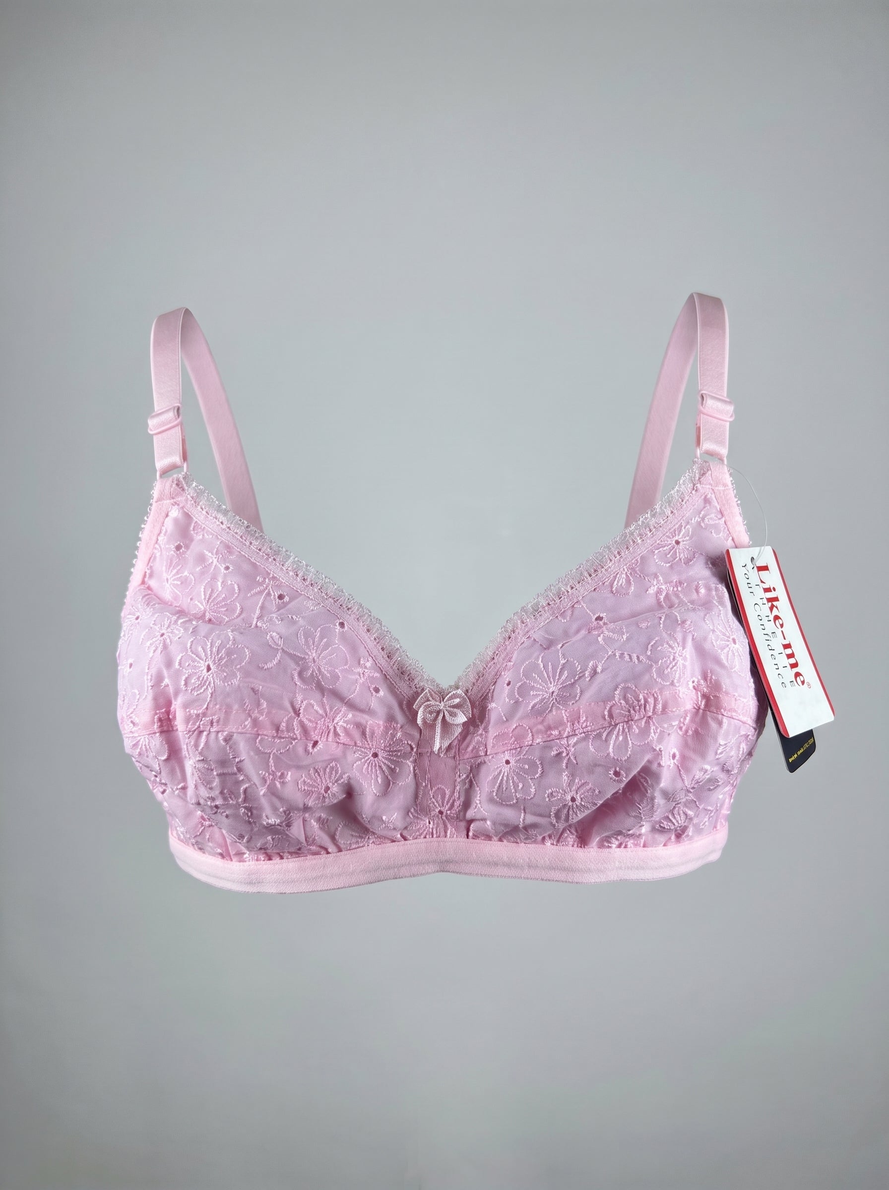 A light pink lace underwire bra with adjustable shoulder straps and a small decorative bow at the center, shown against a neutral gray background with a product tag attached. #color_pink