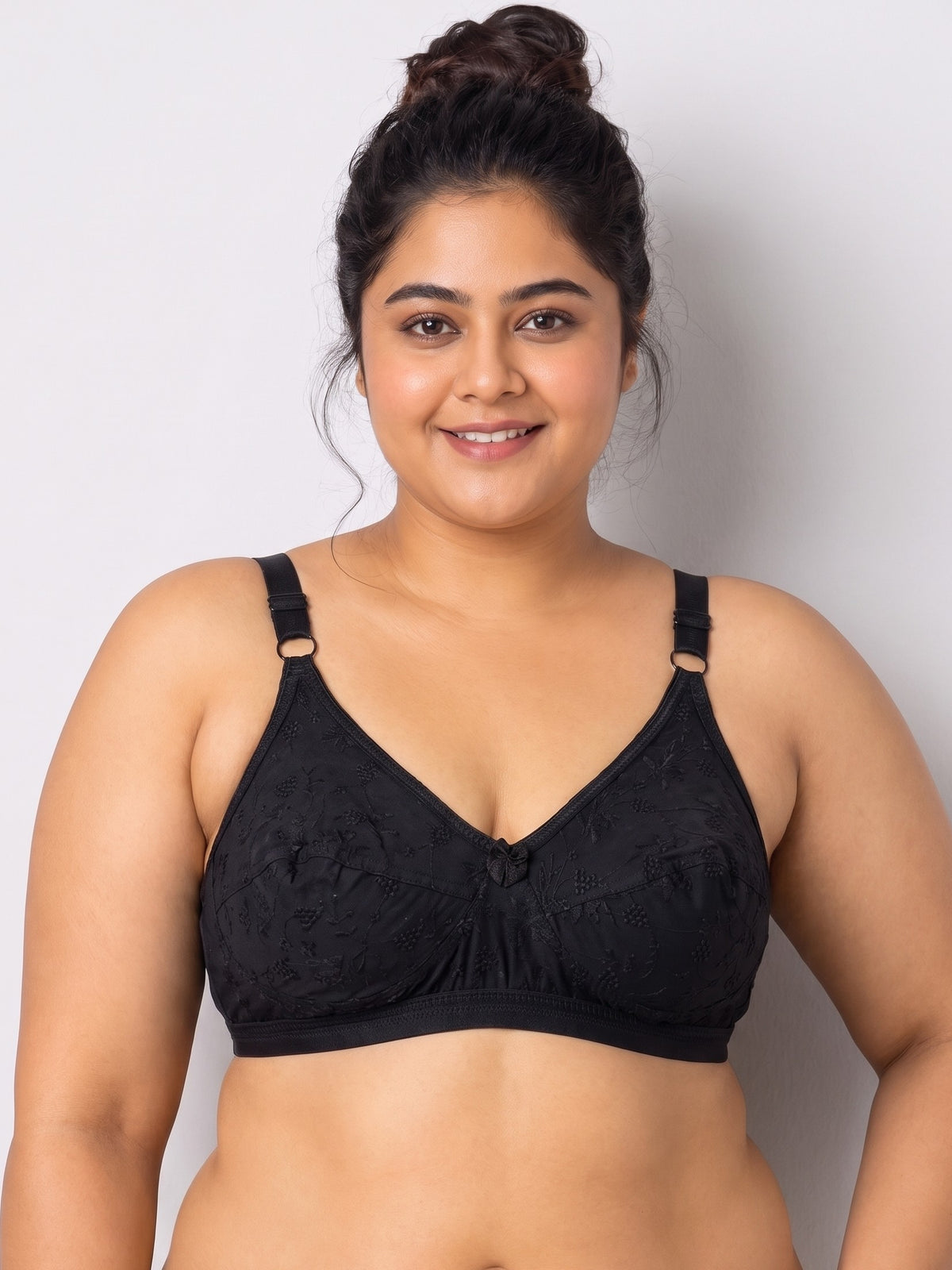 Like-Me Sonu Bra in black with floral lace cups, center bow and adjustable straps, front view on plus-size model. #color_black