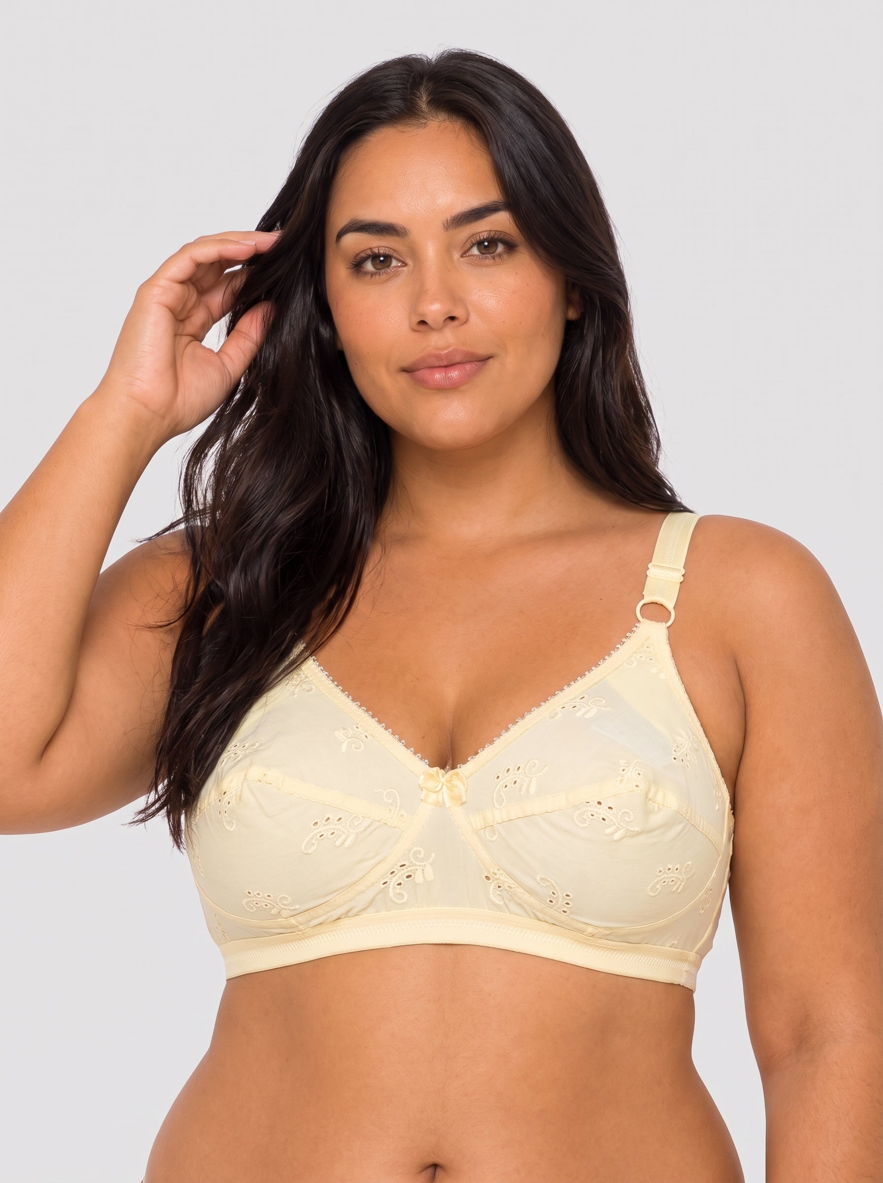 A woman modeling a light cream-colored underwire bra with lace detailing and a single adjustable shoulder strap, set against a solid light gray background. #color_cream