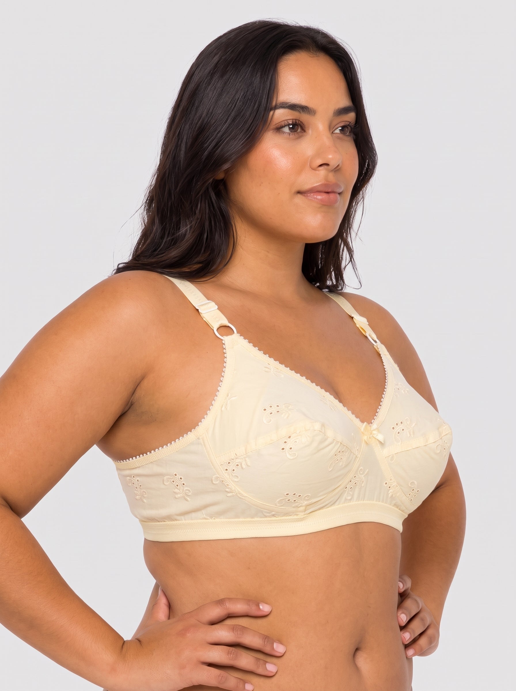 A woman modeling a light cream-colored underwire bra with scalloped edges and eyelet embroidery against a light gray studio background. #color_cream