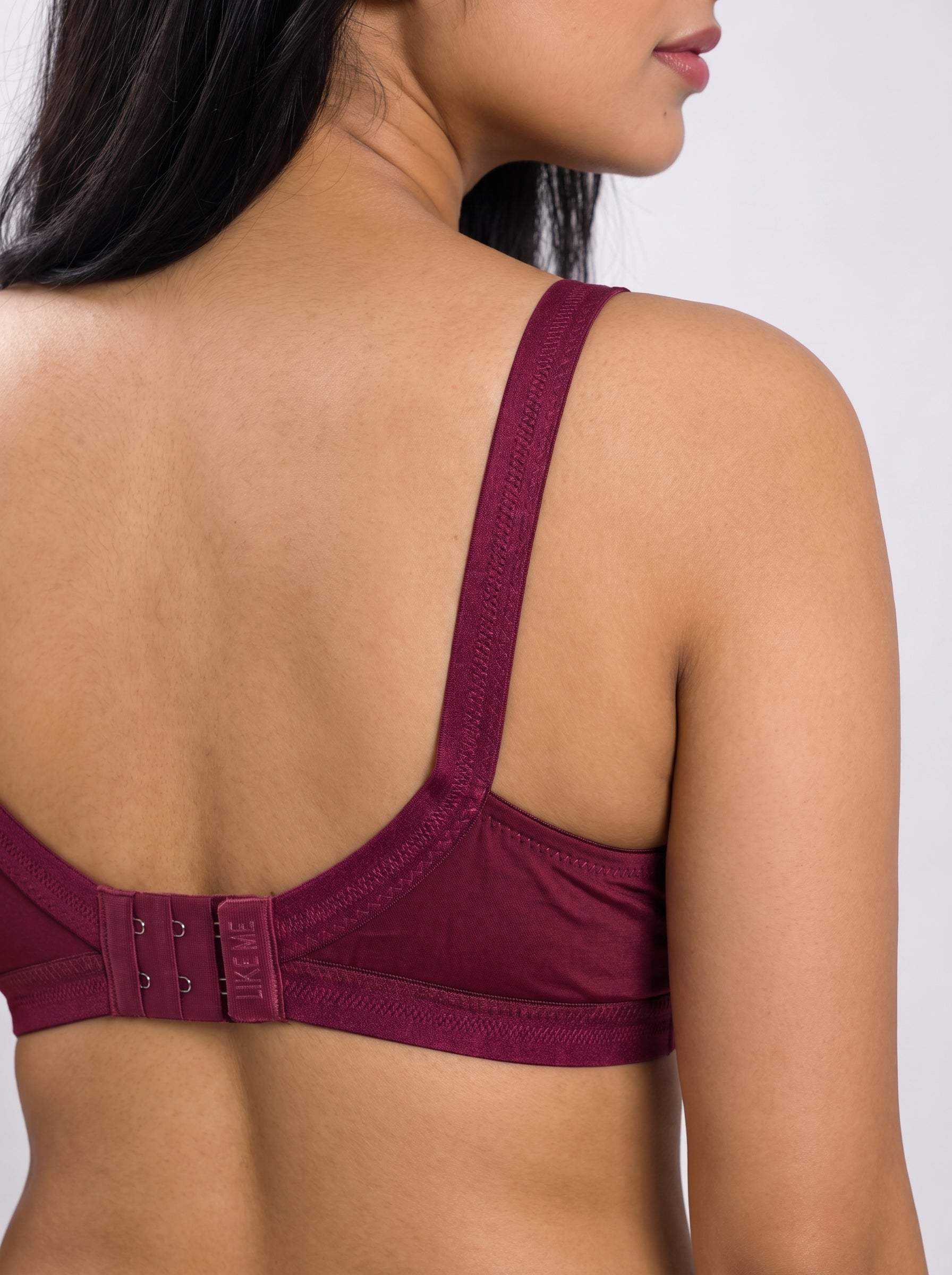 Close-up back view of a woman wearing a burgundy bra, showing the adjustable hook-and-eye back closure and wide shoulder straps against a light gray background. #color_maroon