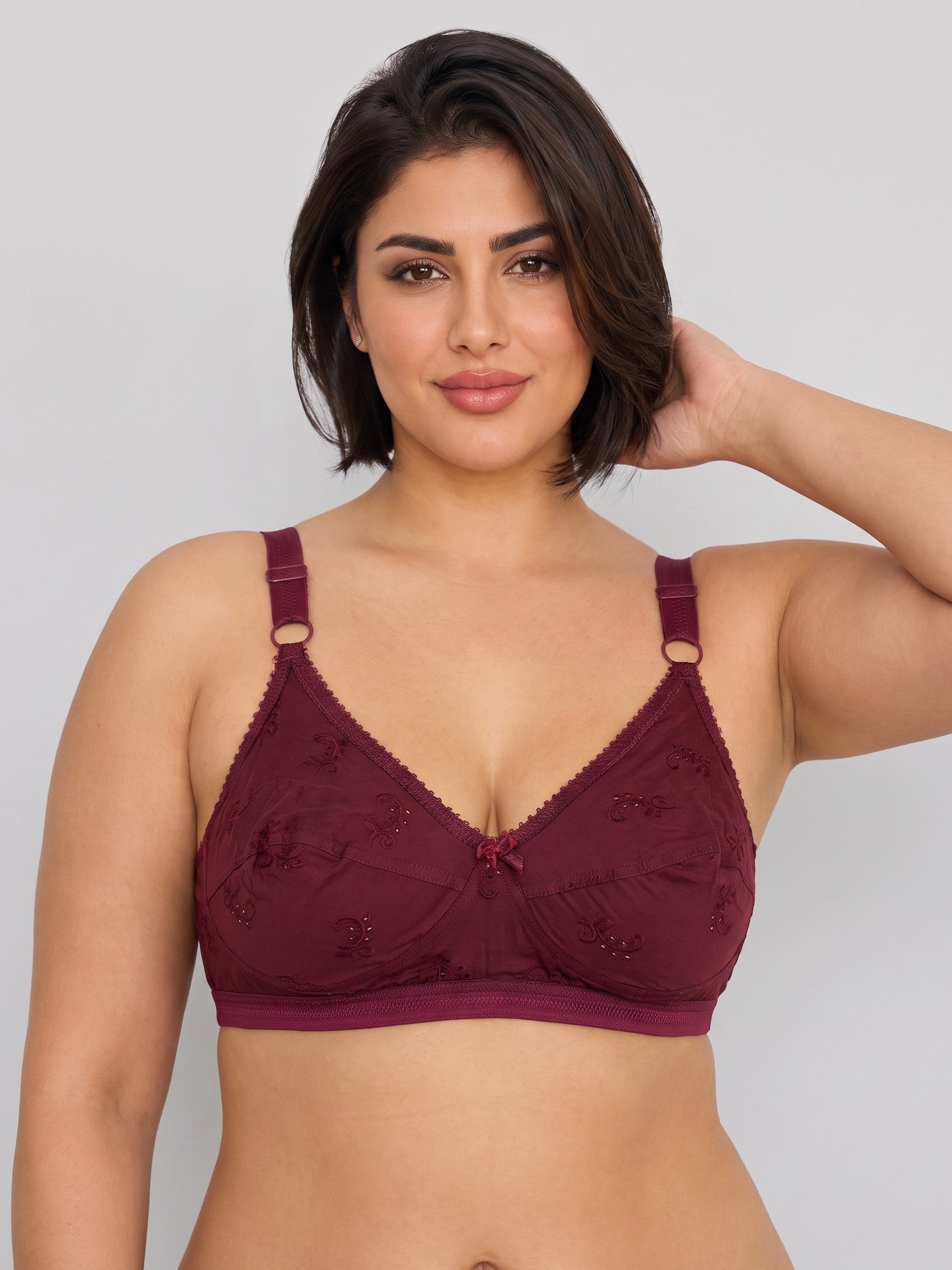 A woman modeling a burgundy lace underwire bra against a light gray studio background. #color_maroon