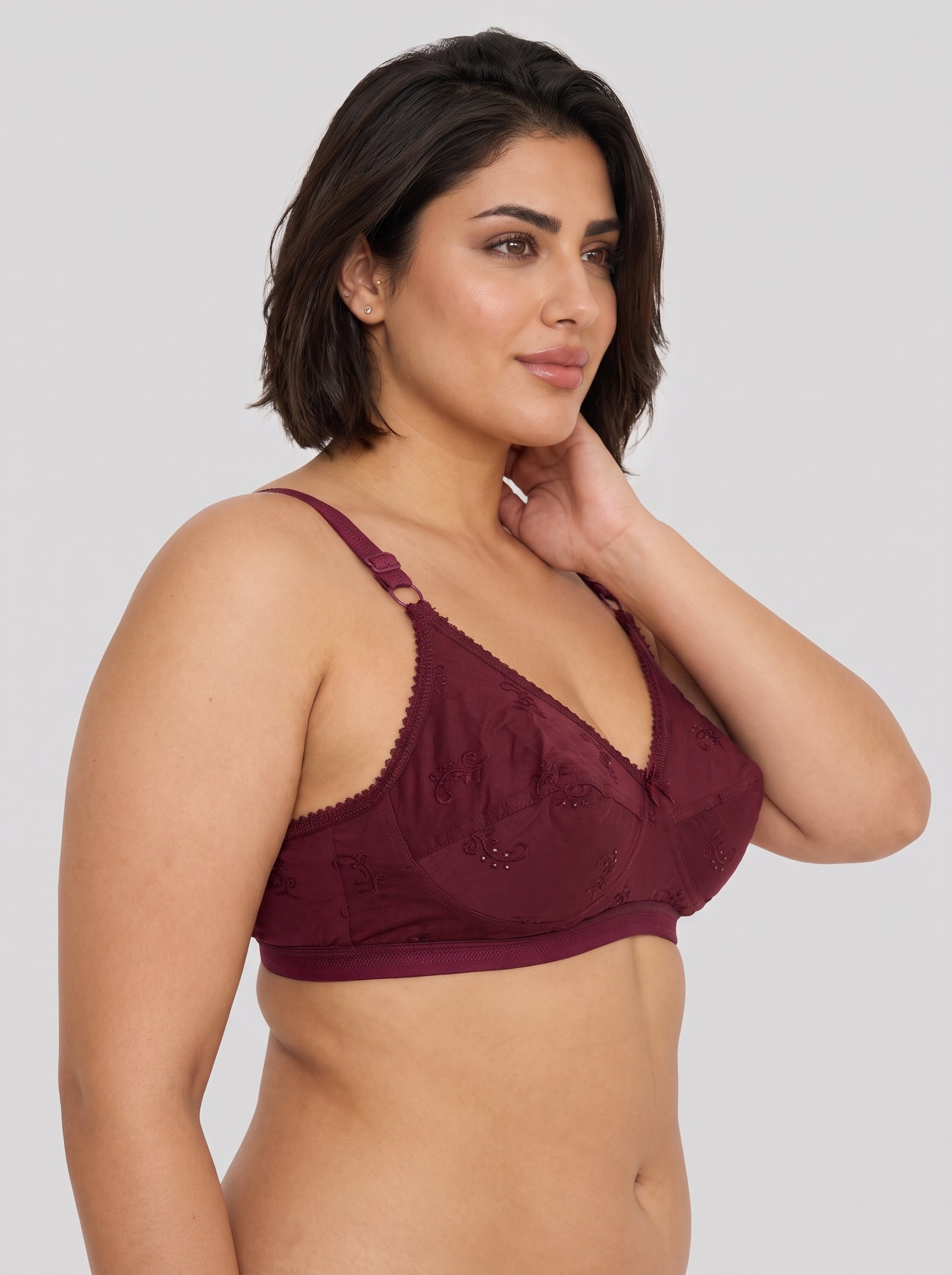 A woman modeling a burgundy lace bralette against a solid light gray background. #color_maroon