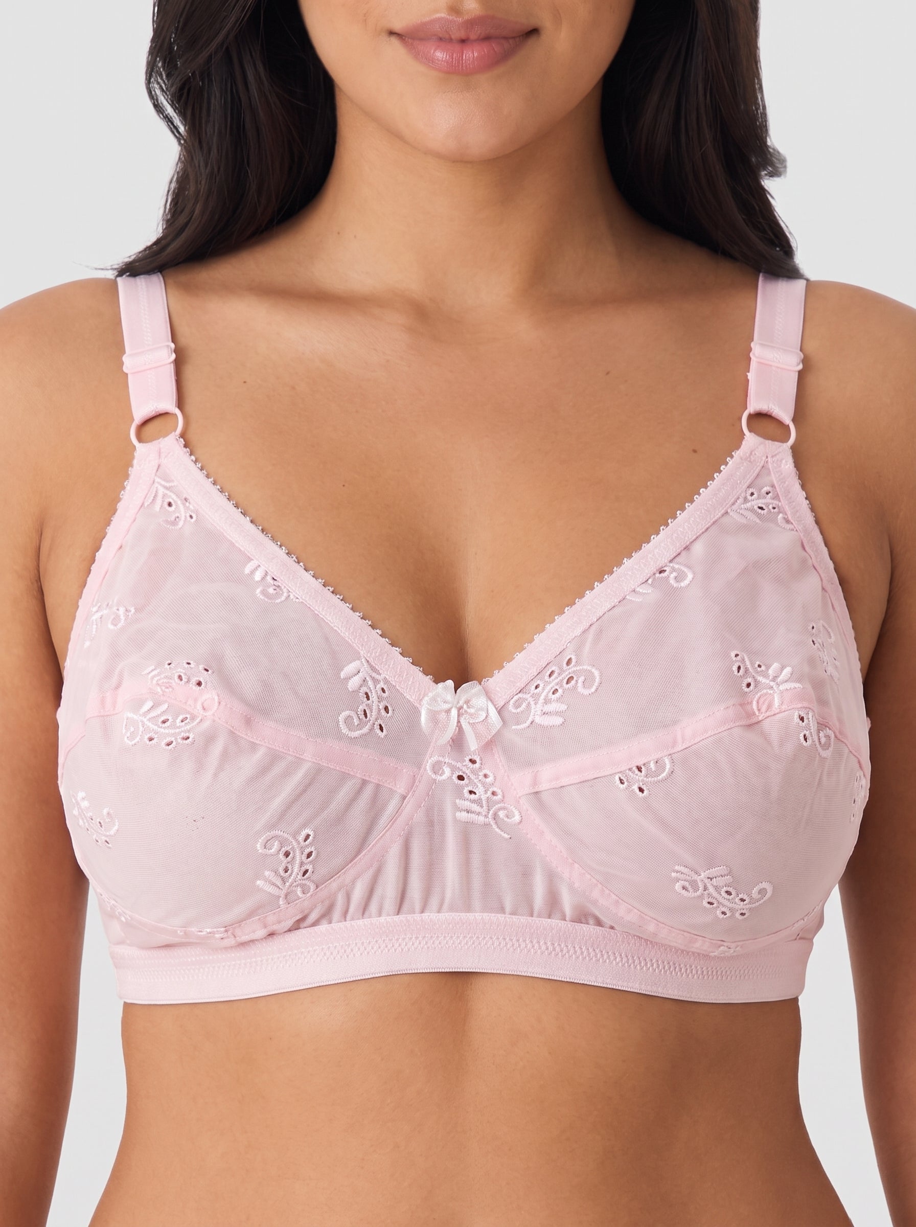 A close-up of a model wearing a light pink underwire bra with floral eyelet embroidery and adjustable shoulder straps. #color_pink