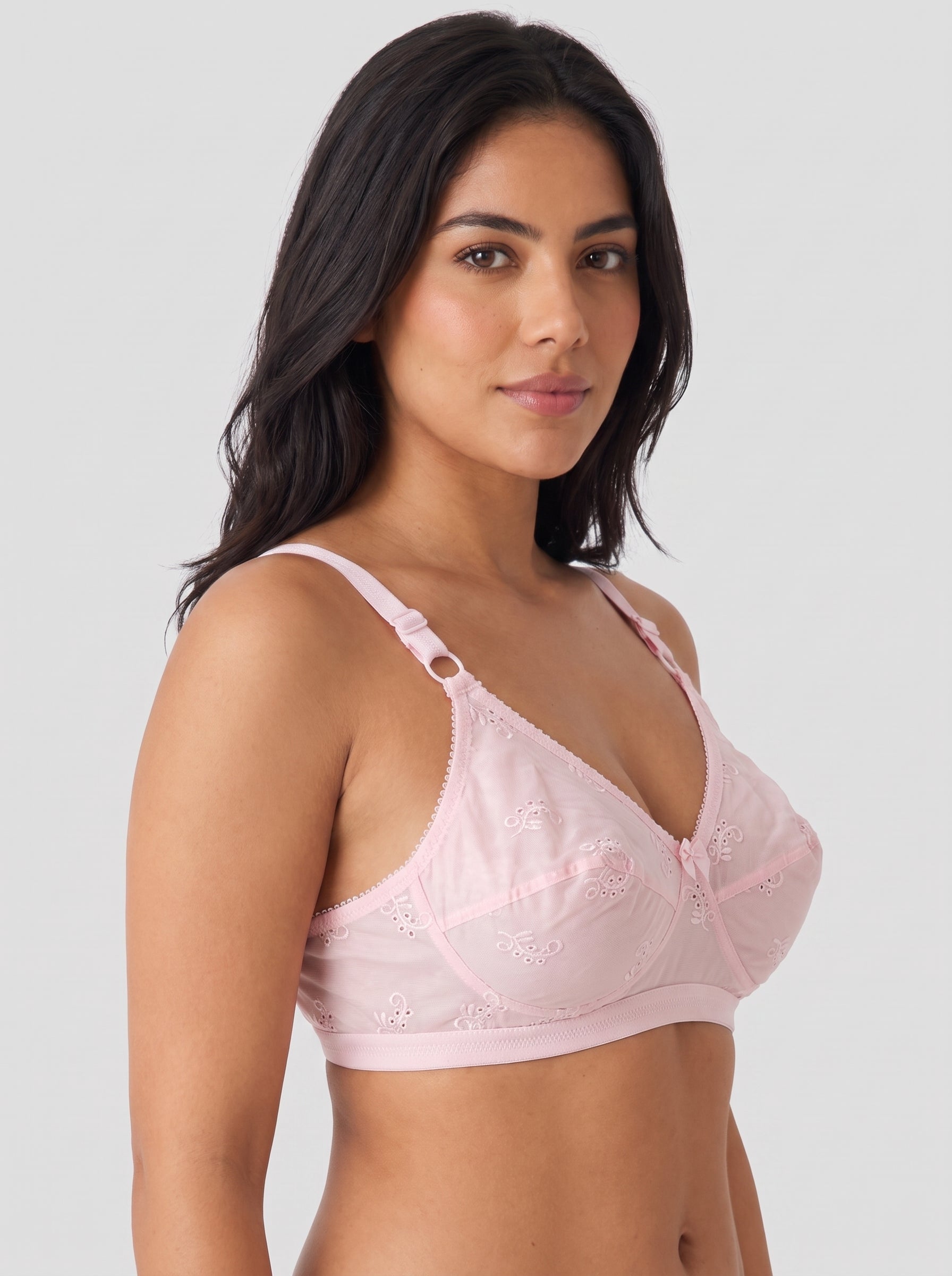 A woman modeling a light pink underwire bra with lace detailing and adjustable shoulder straps, photographed against a solid light gray background. #color_pink