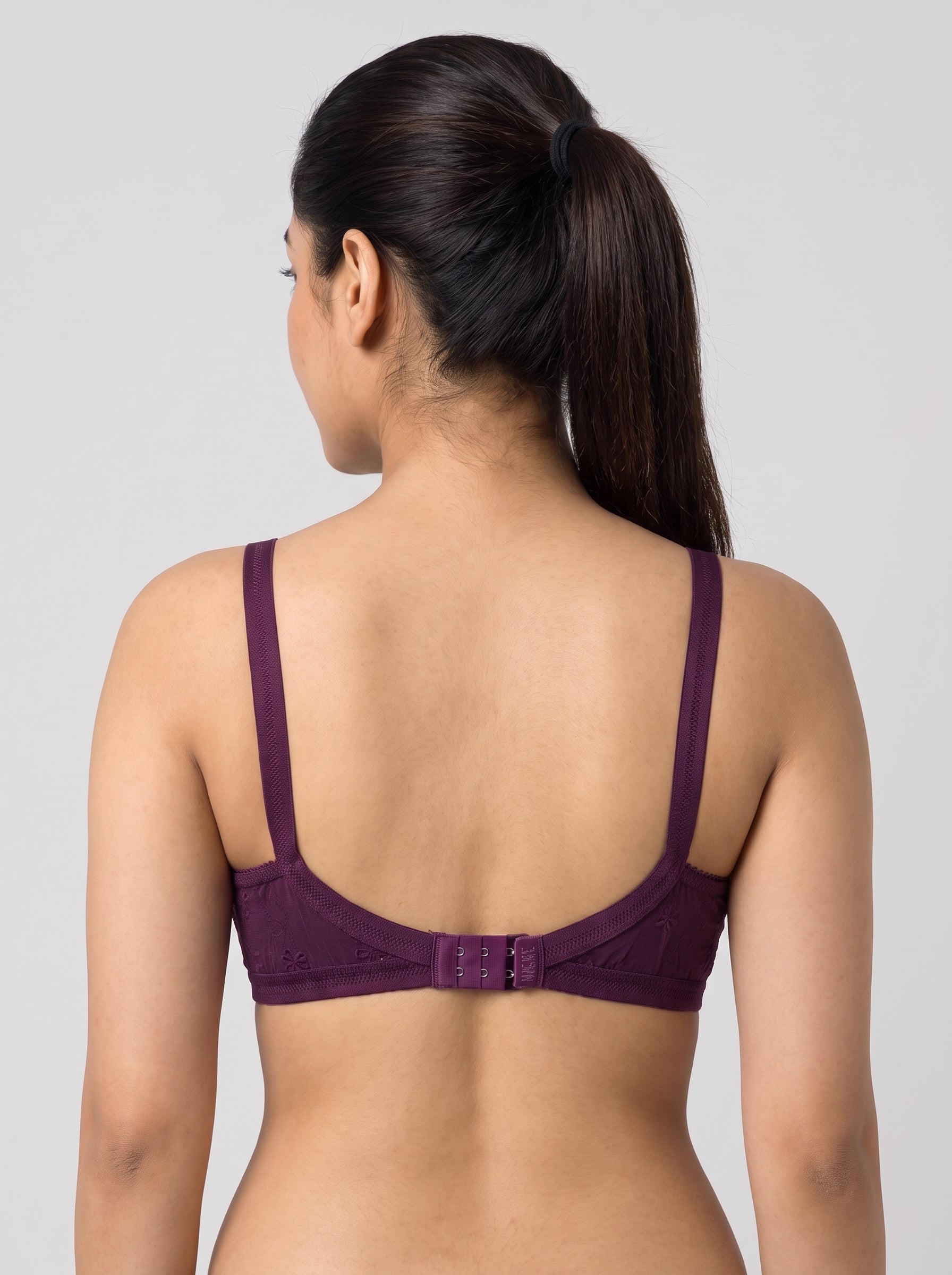 A woman shown from the back wearing a dark purple bra with a low-rise back design and a central hook-and-eye closure, set against a plain light gray studio background. #color_wine