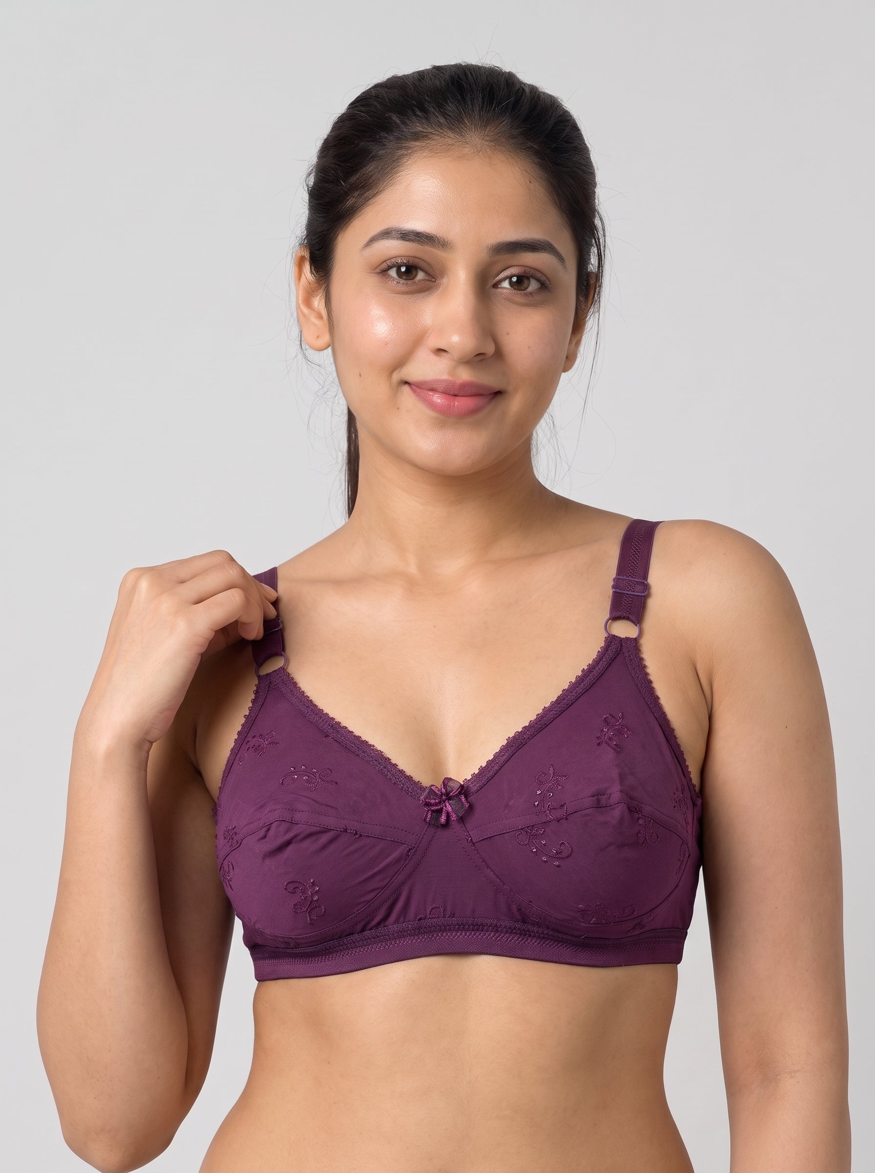 A woman modeling a deep purple lace-trimmed bralette with underwire and adjustable straps against a solid light gray background. #color_wine