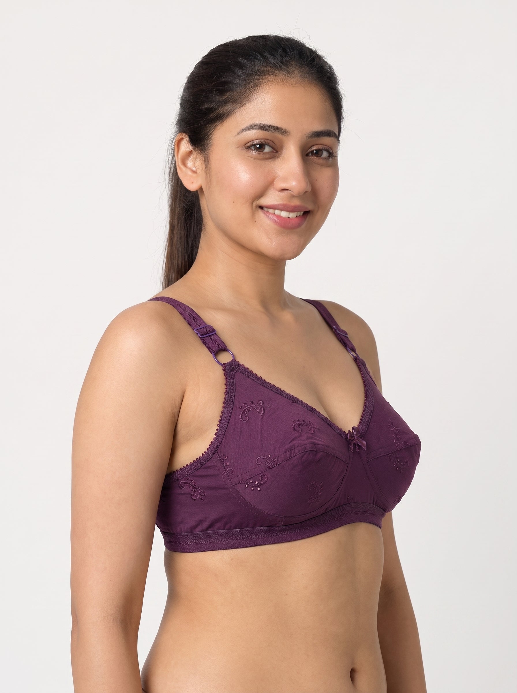 A woman modeling a deep purple lace bralette against a plain light gray studio background. #color_wine