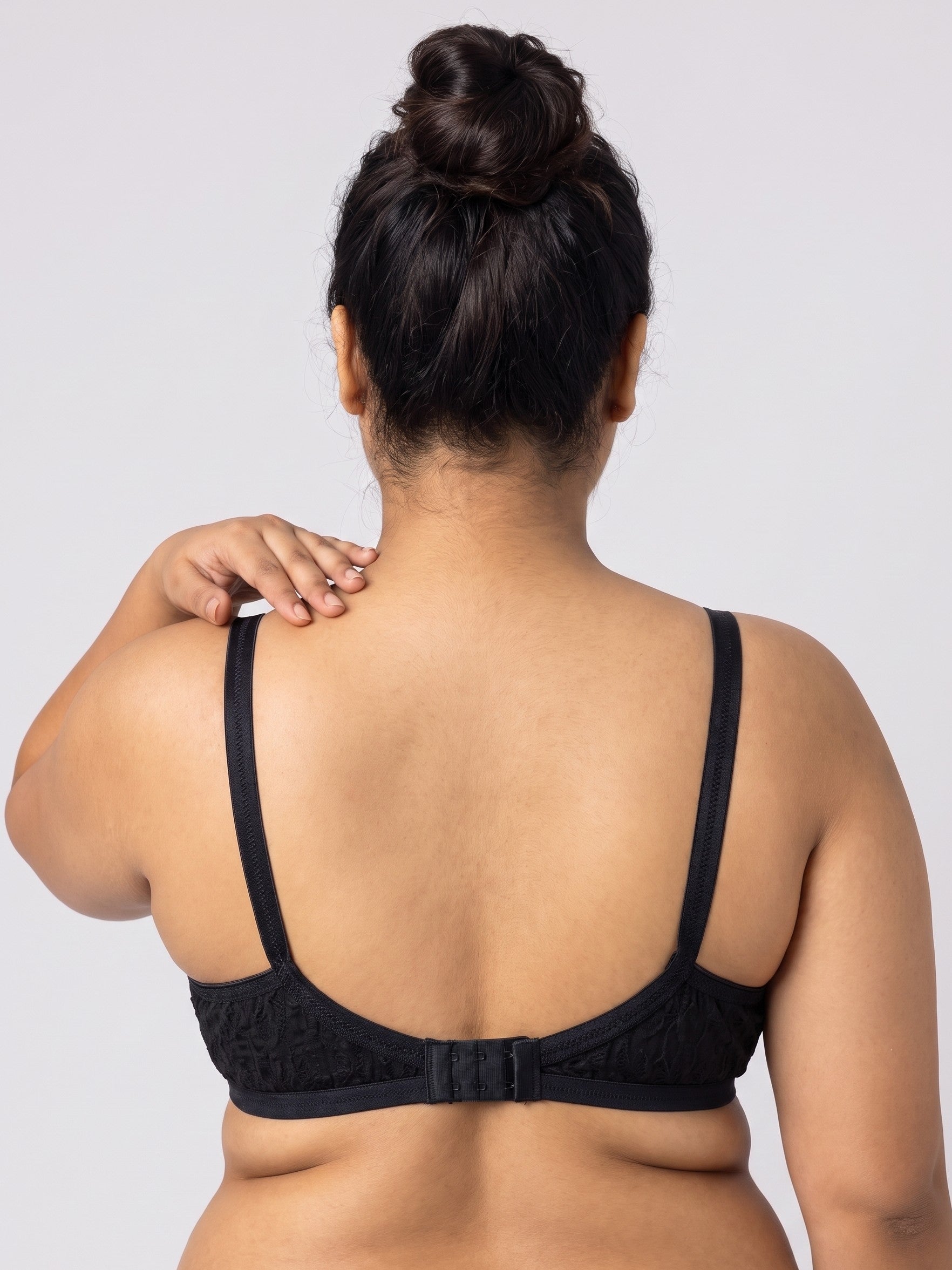 A woman shown from the back wearing a black lace-trimmed bra with thin straps and a center back strap, photographed against a light gray studio background. #color_black