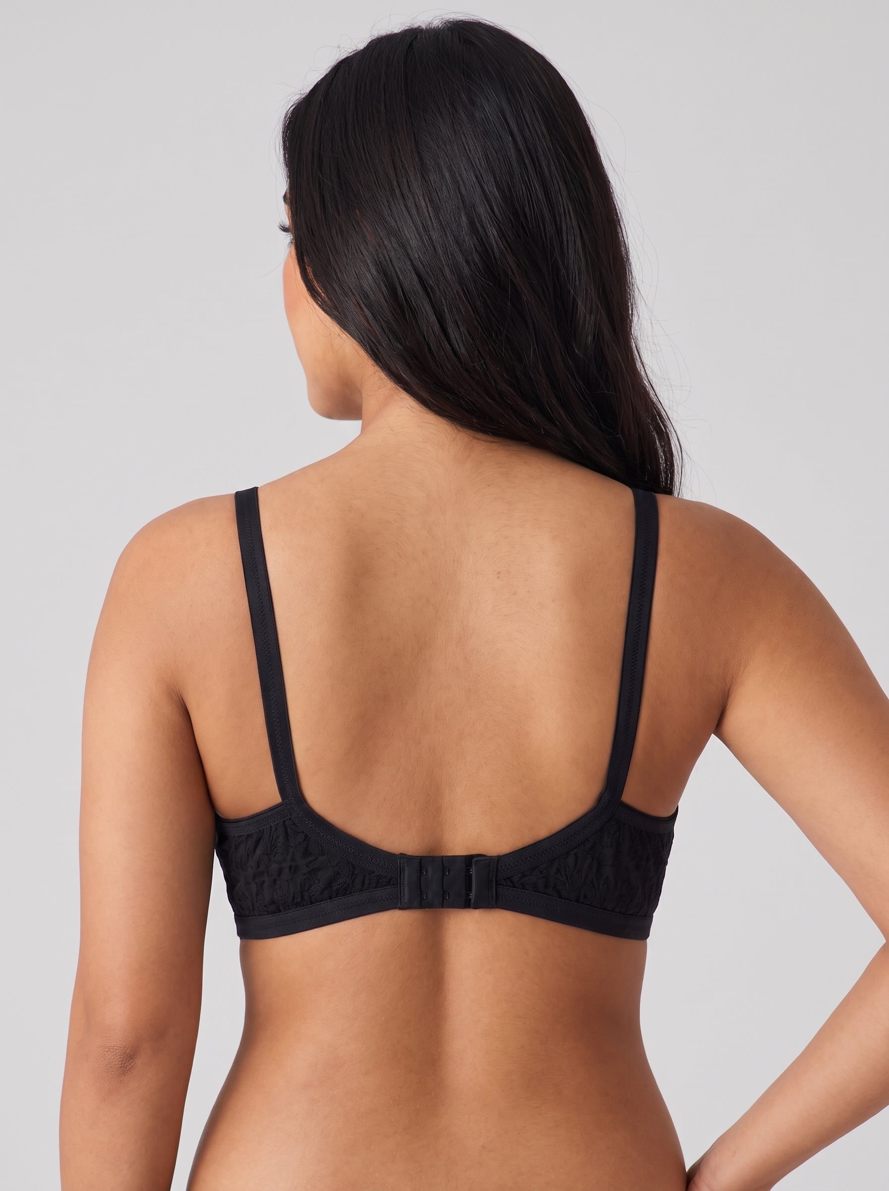 Rear view of a woman wearing a black lace underwire bra with thin shoulder straps and a center back strap, shown against a light gray studio background. #color_black