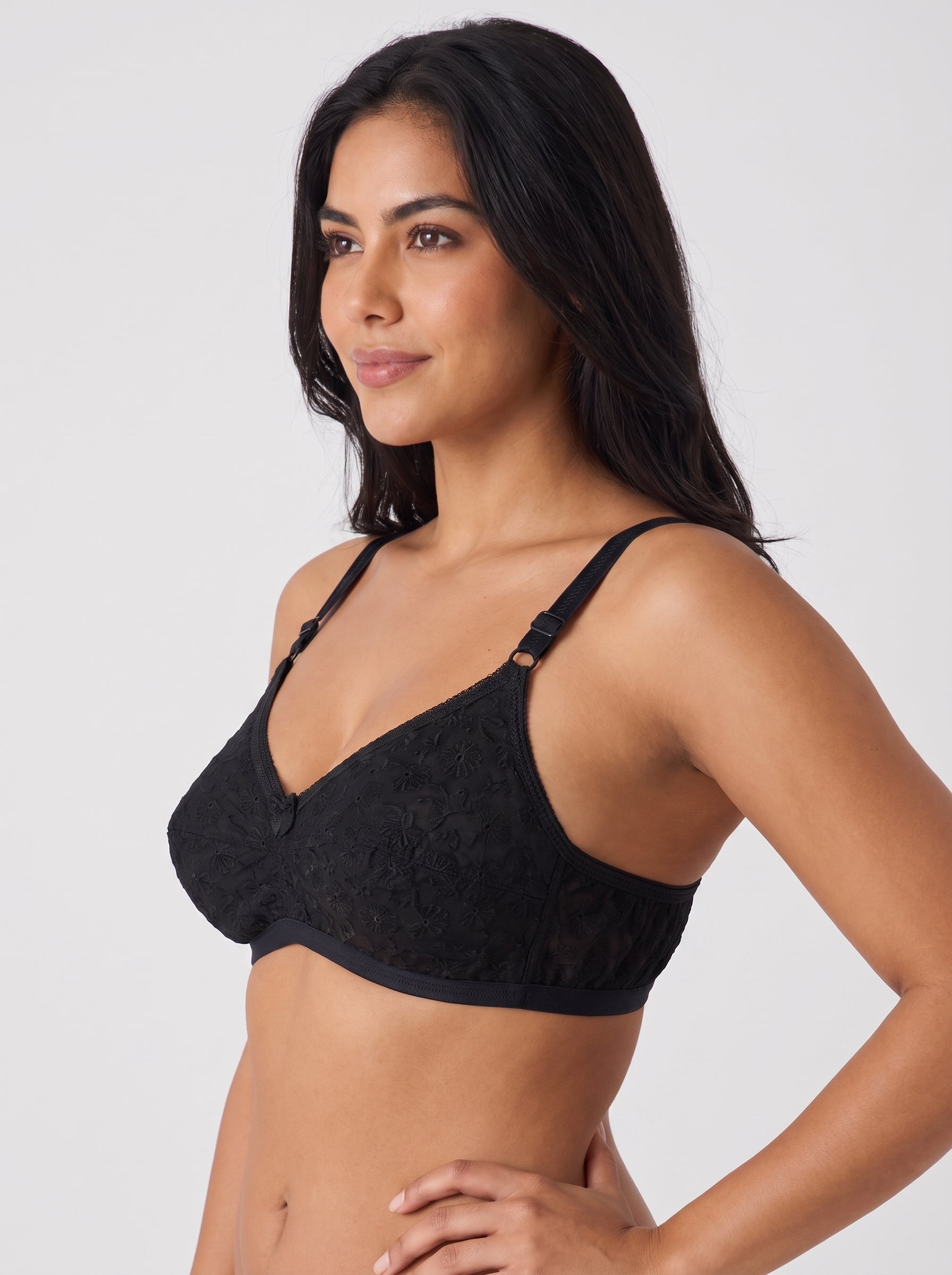 A woman modeling a black lace underwire bra with adjustable shoulder straps against a light gray studio background. #color_black