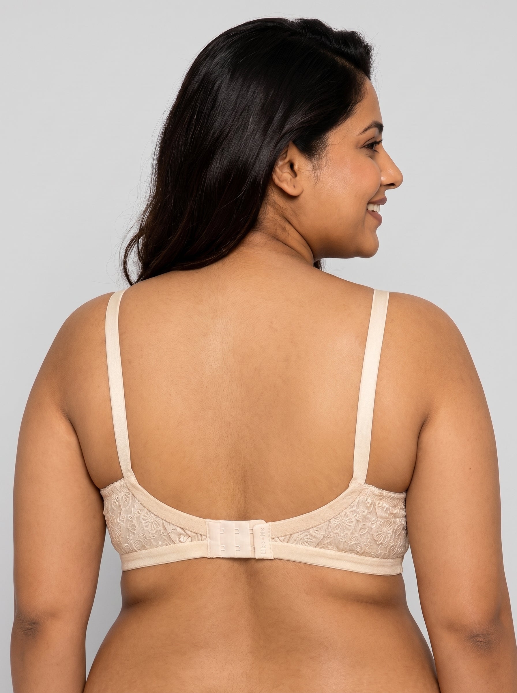 A woman shown from the back wearing a beige lace bra with thin straps and a center back strap detail, against a solid light gray background. #color_cream