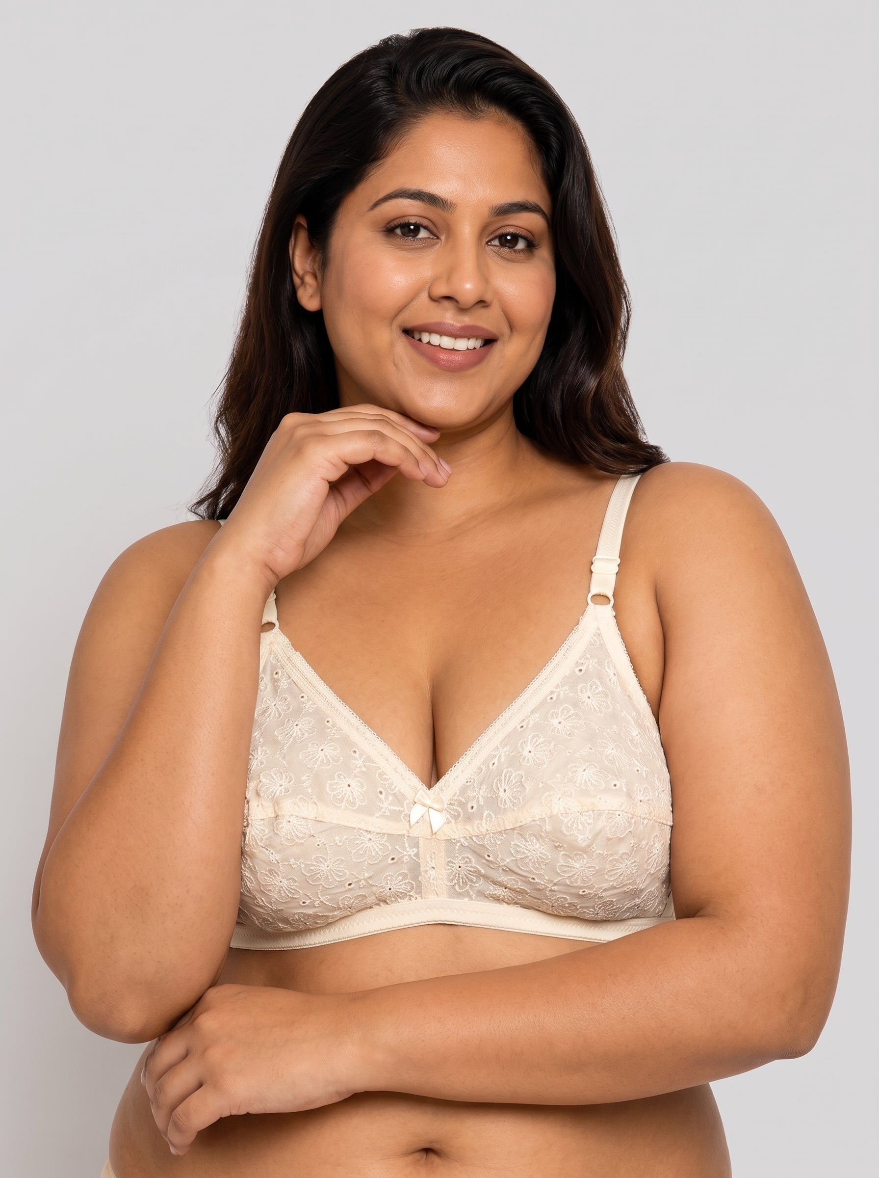 A woman modeling a cream-colored lace bralette against a solid light gray background. #color_cream