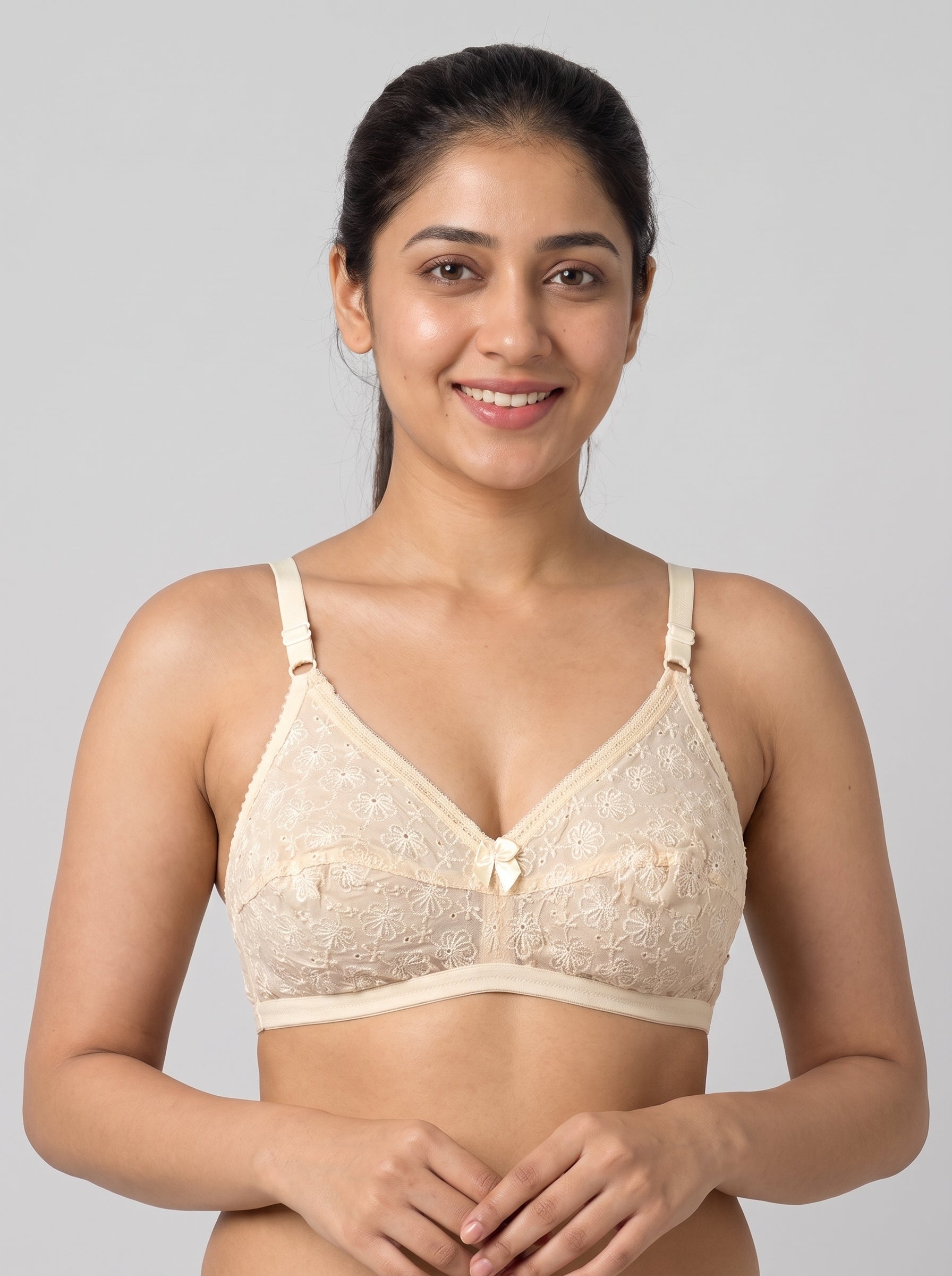 A woman modeling a beige lace bralette against a solid gray studio background. #color_cream