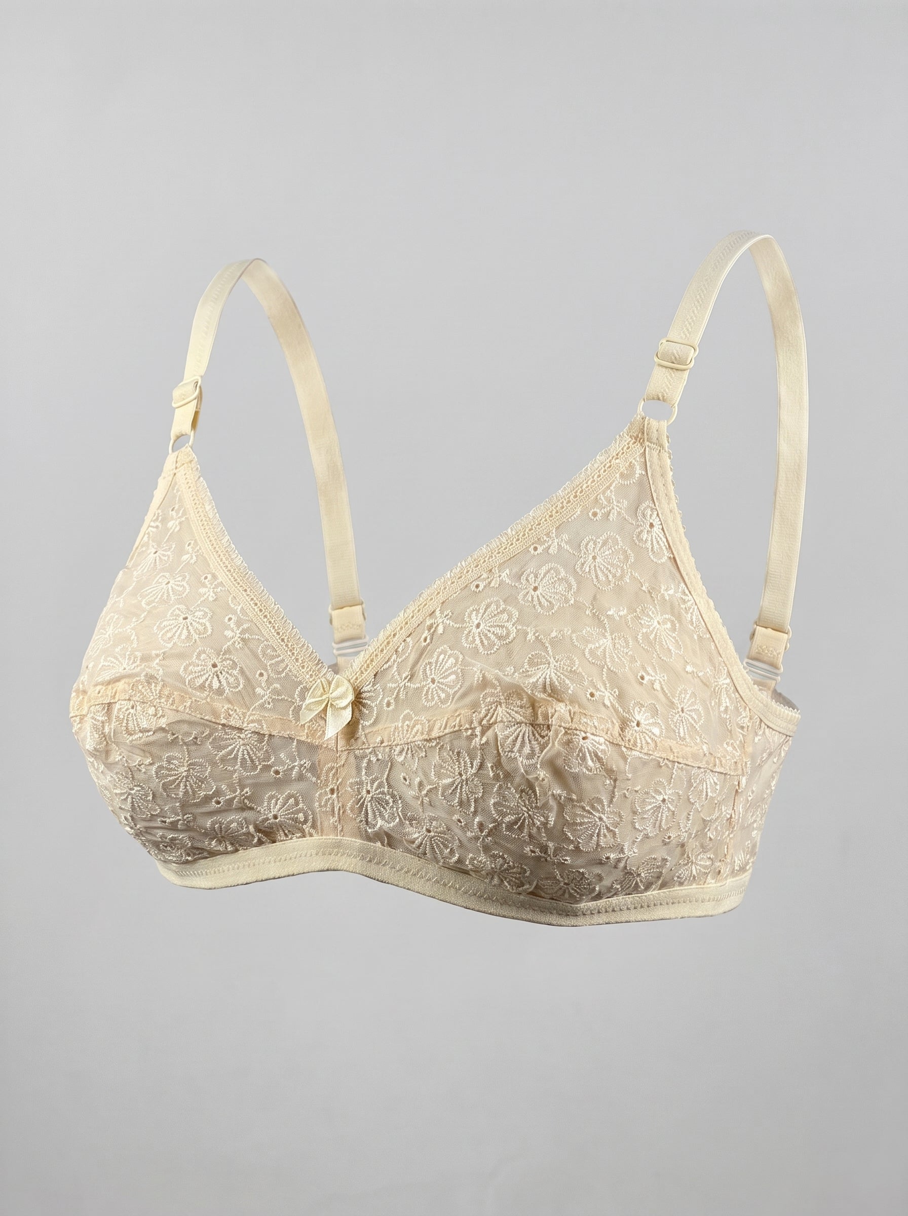 An ivory lace underwire bra with adjustable shoulder straps and a small decorative bow at the center front, shown against a solid gray background. #color_cream