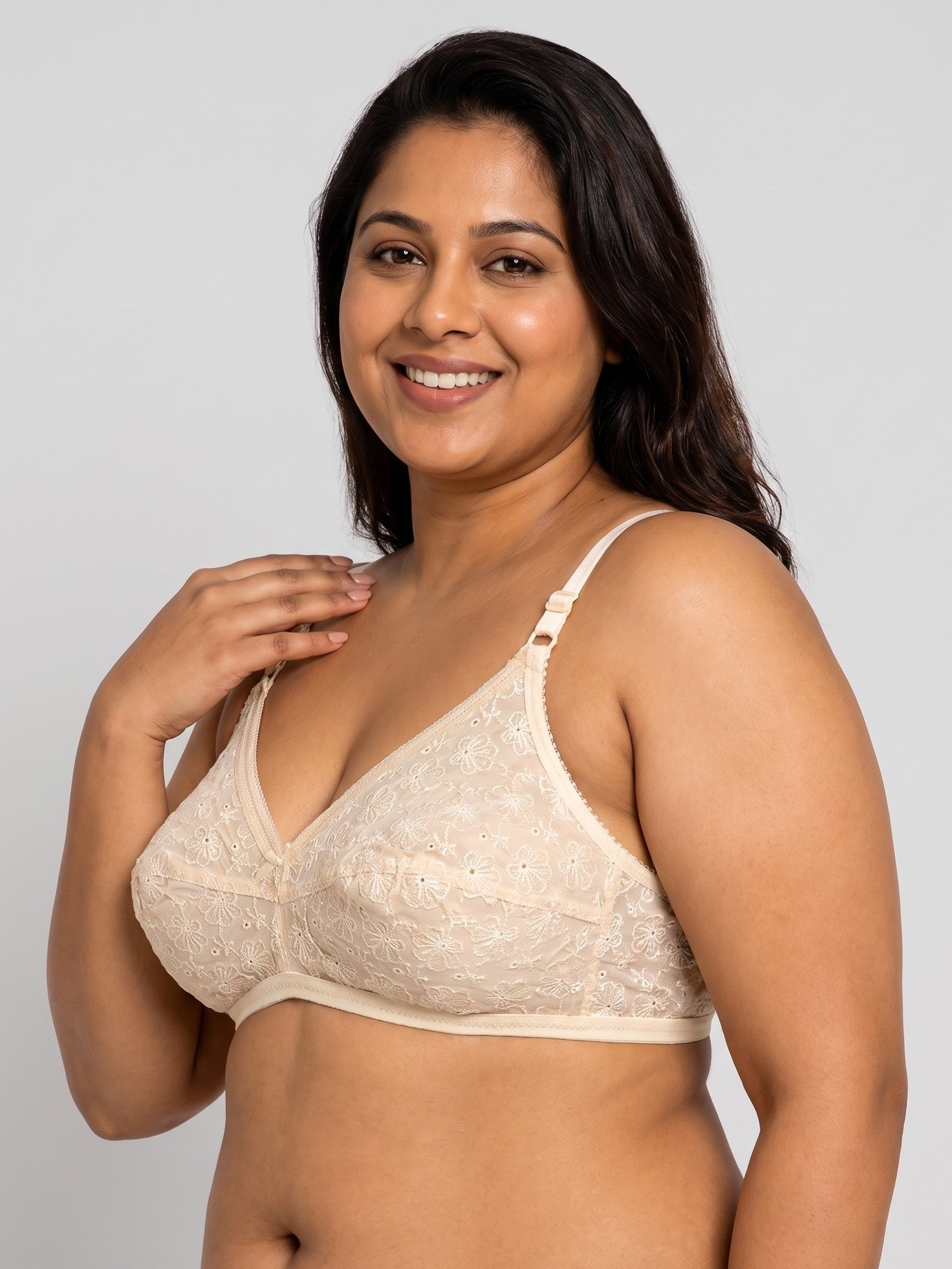 A woman modeling a light beige lace bra against a solid light gray studio background. #color_cream