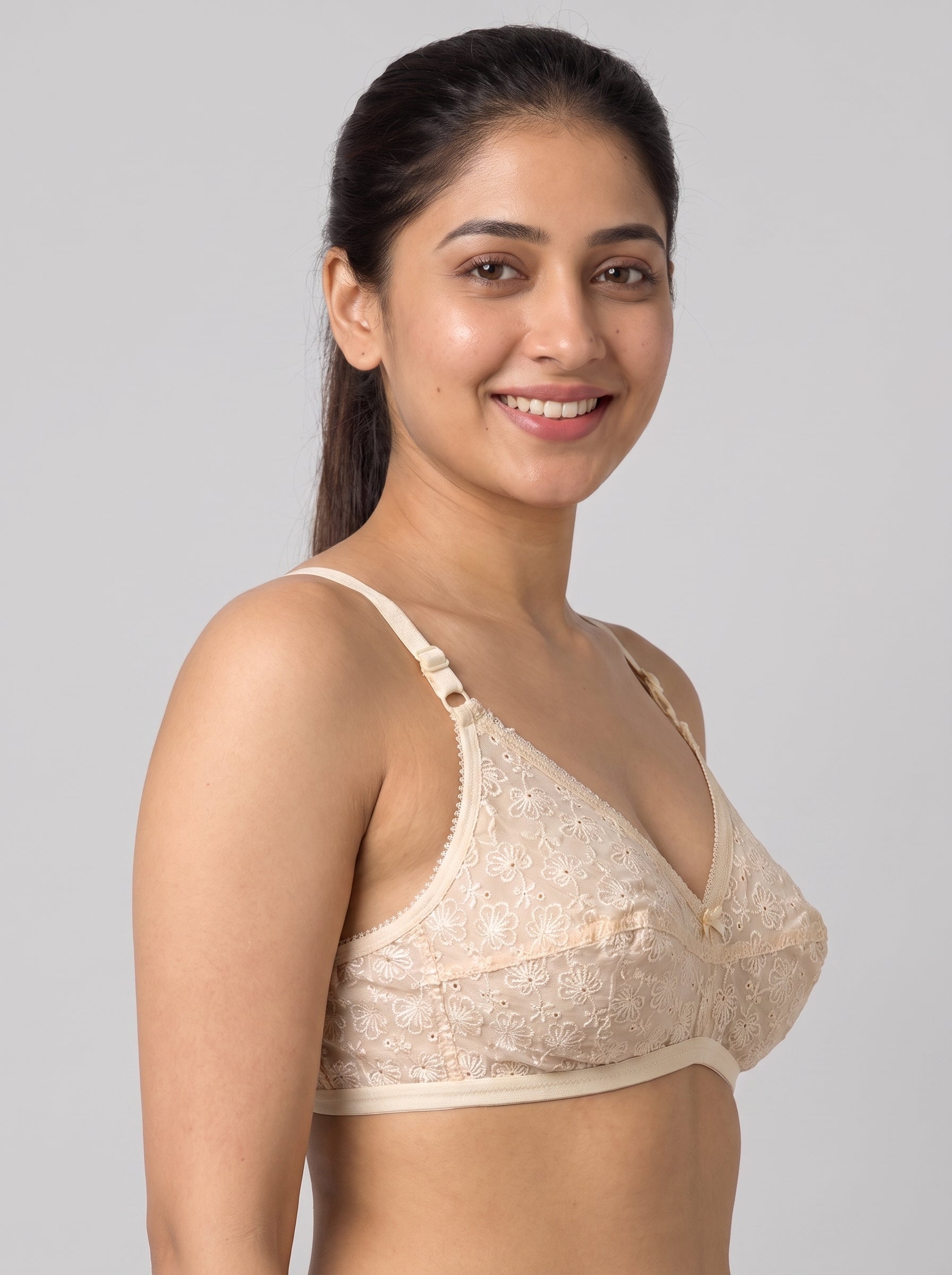 A woman wearing a beige lace underwire bra, shown from the chest up against a solid gray studio background. #color_cream